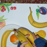 Zdjęcie przedstawia proces robienia animacji poklatkowej z owoców i wycinanek
