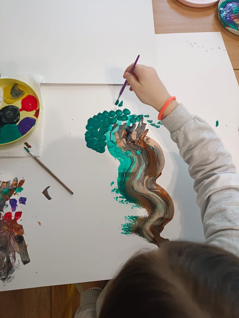 Foto przedstawia dokumentację warsztatów plastycznych. Dzieci malują pędzlami i dłońmi, jest bardzo kolorowo.