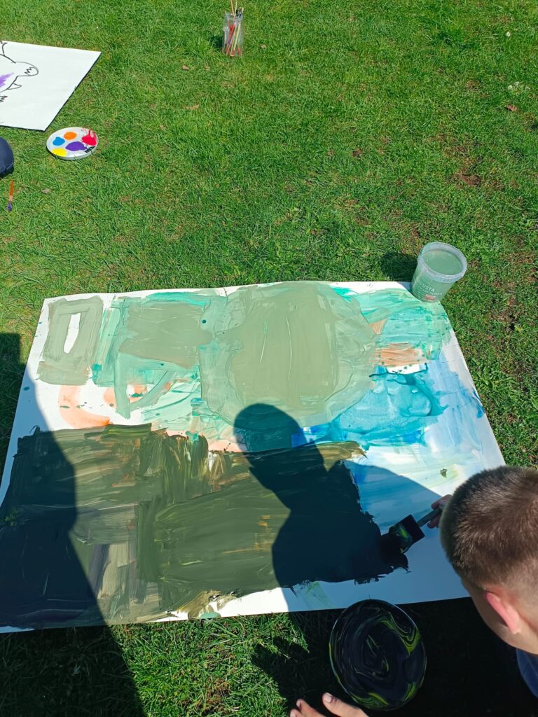 warsztaty plastyczne na zewnątrz, wszyscy malują obrazy na trawie w słoneczku