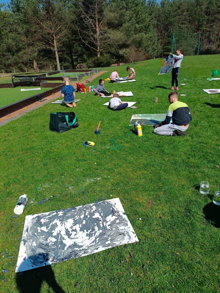 warsztaty plastyczne na zewnątrz, wszyscy malują obrazy na trawie w słoneczku